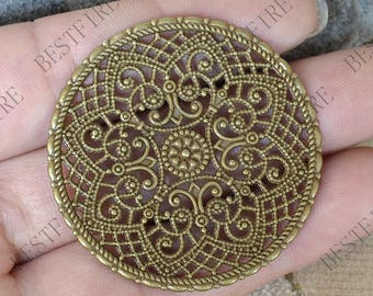 May include: A gold-toned metal filigree charm with a circular design. The charm features intricate, detailed patterns and a delicate, openwork style.