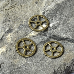 Puede incluir: Tres engranajes de metal de color dorado antiguo con un diseño de estrella de cinco puntas. Los engranajes están sobre una superficie gris texturizada.