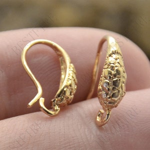 Puede incluir: Dos ganchos para pendientes de color dorado con un diseño texturizado ligeramente curvado. Los ganchos tienen un pequeño bucle en la parte superior para sujetar joyas.