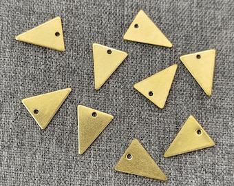 Op de afbeelding: Acht gouden driehoekvormige bedels met een gat in het midden. De bedels zijn in een halve cirkel op een grijze stoffen achtergrond gerangschikt.