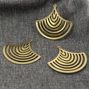 May include: Three gold metal fan-shaped pendants with a geometric design. The pendants have a layered look with concentric circles.