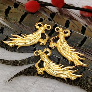 May include: Three gold-colored metal bird-shaped ornaments. Each ornament has a loop at the top and a flowing tail. The ornaments are arranged on a background of brown and black feathers.