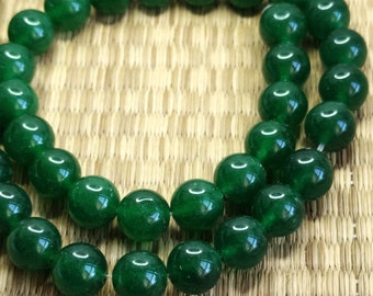 May include: A strand of dark green jade beads, each bead is round and smooth. The beads are strung on a clear thread and are arranged in a circular pattern.