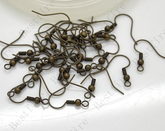 May include: A pile of bronze-colored earring hooks with a spring-loaded closure. The hooks are scattered on a white surface.