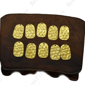 May include: Eight gold-toned metal oval-shaped charms with a hammered texture. The charms have a hole at the top for attaching to jewelry or other crafts.
