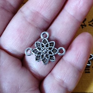 以下が含まれることがあります： ジュエリーやその他のクラフトを付けるための装飾的なマンダラデザインと4つのループが付いた銀色の金属製コネクター