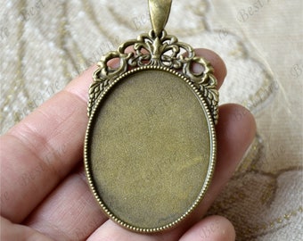 Puede incluir: Un colgante ovalado de bronce con un marco decorativo de filigrana. El colgante tiene una superficie lisa y redonda, perfecta para agregar un diseño personalizado.