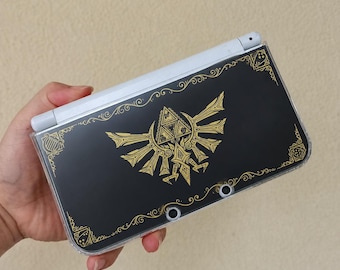 Étui de protection Zelda pour 3DS XL à personnaliser, orné de l'emblème doré d'Hyrule, d'illustrations fantastiques noires et d'un symbole sacré. Un cadeau inspiré de l'aventure.