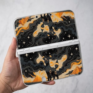 May include: A handheld gaming console featuring a protective skin with a black and orange illustration of a fox-like creature. The design includes swirling dark clouds, glowing stars, and pyramid structures against a starry night sky background.