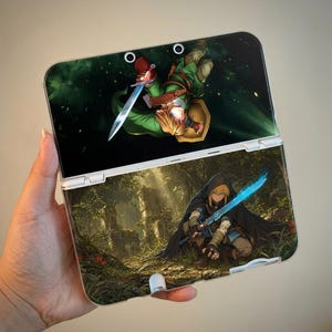 Può includere: Una console di gioco portatile con una skin personalizzata che presenta due distinte illustrazioni fantasy. Lo schermo superiore mostra un personaggio in verde che impugna una spada, mentre la sezione inferiore raffigura una figura incappucciata.