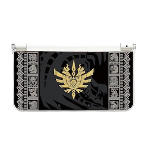 Könnte beinhalten: Eine schwarze und goldene Nintendo 3DS-Hülle mit einem stilisierten Emblem und dekorativen Mustern. Die Hülle hat ein weißes Scharnier und eine transparente Kunststoffabdeckung. Das Design umfasst ein zentrales goldenes Emblem und sich wiederholende geometrische Muster.