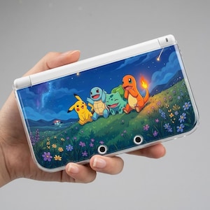Può includere: Una console di gioco portatile bianca con una custodia protettiva trasparente decorata con un grafico di Pikachu, Squirtle, Bulbasaur e Charmander in un campo fiorito sotto un cielo notturno stellato e colline in lontananza.