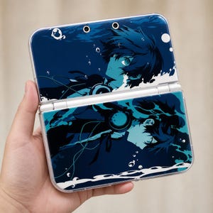 Könnte beinhalten: Eine blau-weiße Nintendo 3DS-Hülle mit einer Anime-Illustration einer Person unter Wasser. Die Hülle ist geöffnet und zeigt den Bildschirm und die Tasten. Das Design umfasst Blasen und ein dunkelblaues Farbschema.
