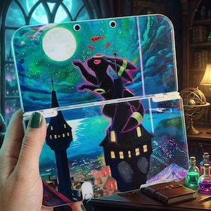 May include: A handheld gaming console featuring a vibrant graphic of a black creature with glowing yellow rings perched atop a dark tower under a full moon. The scene includes a starry night sky, a distant landscape, and a castle-like structure.