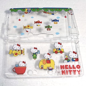 May include: Clear plastic case with Hello Kitty illustrations. The design includes Hello Kitty in various vehicles and settings, such as airplanes, a motorcycle, and an elephant. The words "HELLO KITTY" are printed in red.