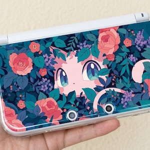 May include: A white and teal handheld gaming console featuring a floral design with pink roses, purple flowers, and green leaves. A cartoon character with pink skin and blue eyes is centered on the console.