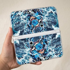May include: A handheld gaming console featuring a vibrant graphic of a blue, turtle-like creature with cannons on its back, surrounded by splashing ocean waves, bubbles, and a dark, stormy sky. The design covers both the top and bottom panels.