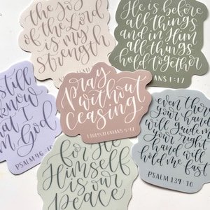 May include: A collection of six die-cut stickers with inspirational quotes in elegant calligraphy. The stickers feature pastel colors like lavender, sage green, and dusty rose. Each sticker displays a different quote from the Bible.
