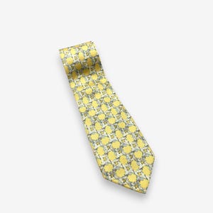 May include: A yellow necktie with a repeating pattern of yellow circles and small gray and white floral accents. The tie is angled diagonally across a white background.