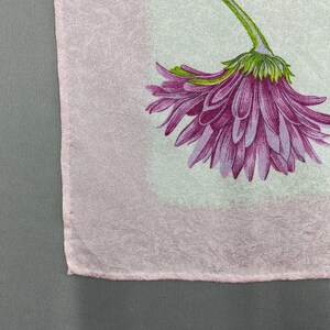 Puede incluir: Un textil rosa claro con un gran estampado floral morado detallado. La flor tiene un tallo y una base verdes, con p&eacute;talos en varios tonos de morado. El textil tiene un aspecto sutil y texturizado.