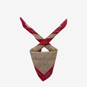 May include: A tan and red bandana with a horseshoe and chain pattern. The bandana has a red border and red stripes on the folded ends. The text "by Polo Gucci" is visible on the border.
