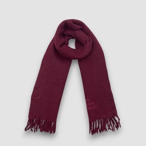 May include: A burgundy scarf with fringe at the ends. The scarf is made of a soft material and has the brand name embroidered on one end. The scarf is a solid color and is suitable for cold weather.