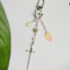 Peut inclure: Un porte-clés argenté avec un charme d'épée, un papillon et des perles pendantes roses, vertes et jaunes. Le porte-clés est doté d'un fermoir à anneau en D pour une fixation facile.