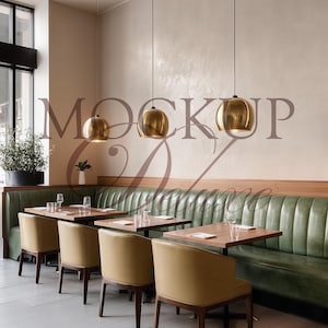Op de afbeelding: Restaurantinterieur met een groene leren bank, houten tafels en beige stoelen. Gouden hanglampen hangen boven de tafels. De muren zijn lichtbeige van kleur en links is een groot raam te zien.