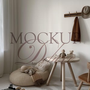 May include: A neutral-toned nursery scene with a round wooden table, a beanbag chair, and a small wooden chair. A coat and hat hang on the wall. A rug and toys are on the floor. The wall has the text "MOCKUP Deluxe".