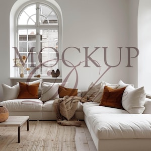 Puede incluir: Un salón luminoso y espacioso con un gran sofá seccional blanco, acentuado con cojines color óxido y crema. Una manta tejida y una mesa de centro de madera añaden calidez. La palabra "MOCKUP" es visible en la imagen.