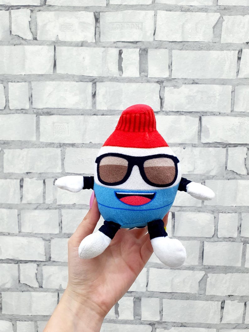 May include: A plush toy shaped like a tube of toothpaste, featuring a red cap, black-framed sunglasses, and a blue and white body. The toy has white arms and legs, and a smiling mouth.