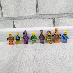 May include: Seven Lego minifigures are displayed. Each figure has a unique design, with various colours including yellow, orange, green, purple, and blue. The figures are arranged in a row against a light grey background.