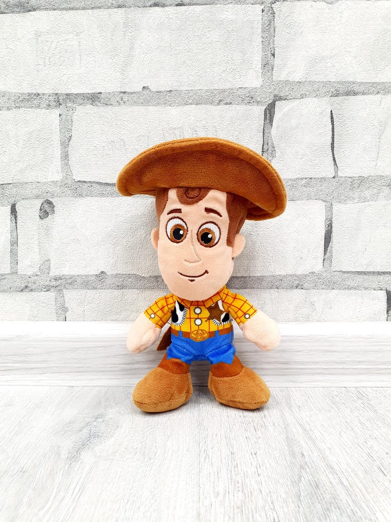K&ouml;nnte beinhalten: Ein Pl&uuml;schtier einer Cartoon-Cowboy-Figur mit braunem Cowboyhut, gelbem kariertem Hemd, blauer Hose und braunen Stiefeln. Das Spielzeug hat einen freundlichen Gesichtsausdruck und steht aufrecht.