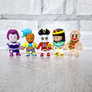 May include: Five colorful figurines in various costumes, including a purple-haired character, a figure with blue hair, a pirate, an Egyptian pharaoh, and a gingerbread man. The figures are standing in a row, each with unique outfits and expressions.