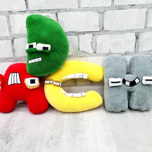 Puede incluir: Una colección de letras del alfabeto de peluche en varios colores. Las letras incluyen A rojo, D verde, C amarillo y H gris. Cada letra tiene una cara con ojos y boca. Los peluches están sobre una superficie de madera clara.