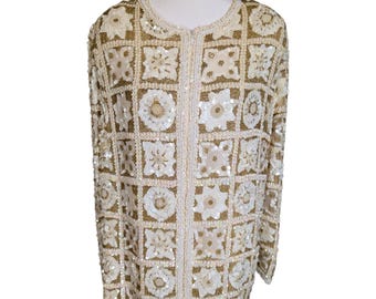 May include: A long-sleeved jacket featuring a grid pattern of alternating square and circular motifs. The garment is heavily embellished with white sequins and gold-toned beads, creating a textured surface. It has a round neckline and a front closure.