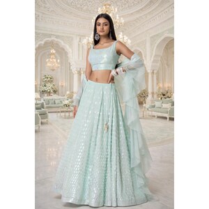 Op de afbeelding: Een lichtblauwe, tweedelige formele outfit. De mouwloze crop top en lange rok zijn versierd met een subtiel patroon. Een doorschijnende, gefranjerde sjaal voegt een delicate touch toe. De outfit is geschikt voor speciale gelegenheden.