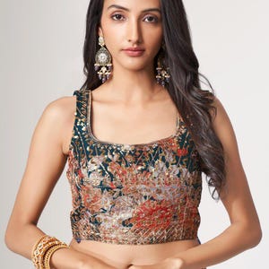 May include: A sleeveless, square-neck top with a floral pattern in shades of teal, orange, and gold. The top is embellished with sequins and paired with matching floral print bottoms. Gold bangles and a large ring with pearls complete the look.