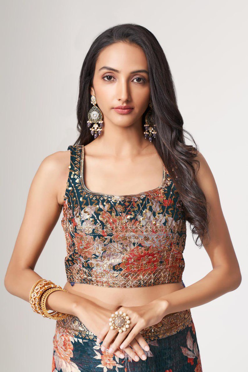 May include: A sleeveless, square-neck top with a floral pattern in shades of teal, orange, and gold. The top is embellished with sequins and paired with matching floral print bottoms. Gold bangles and a large ring with pearls complete the look.