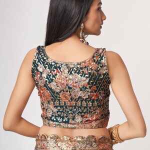 May include: A sleeveless, dark teal top with intricate floral embroidery in shades of orange, gold, and pink. The top features a detailed sequin design and is paired with a matching floral skirt. A gold bracelet and earrings complete the look.