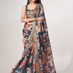 May include: A flowing, floral-print saree in shades of teal, coral, and cream. The saree features a detailed gold border and matching sleeveless blouse. The fabric drapes elegantly, showcasing the intricate floral pattern. A traditional Indian garment.