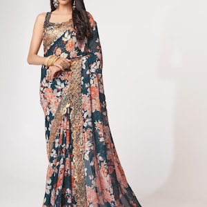 May include: A dark teal floral saree with orange and white blossoms. The saree features a gold embellished border and a matching gold trim along the edges. The fabric drapes elegantly, showcasing the intricate floral pattern.
