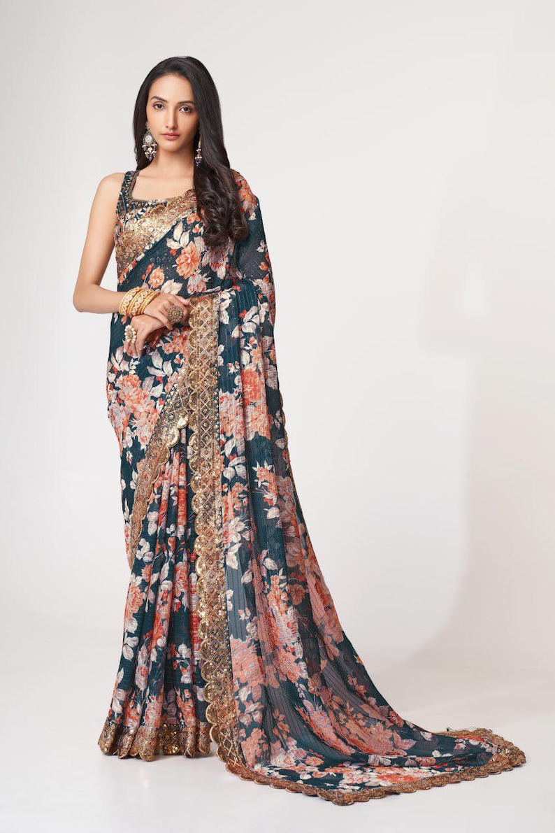 May include: A dark teal floral saree with orange and white blossoms. The saree features a gold embellished border and a matching gold trim along the edges. The fabric drapes elegantly, showcasing the intricate floral pattern.