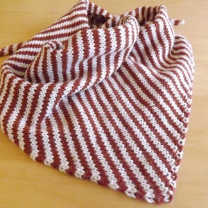 May include: A knitted scarf in a triangular shape, with alternating stripes of white and a deep reddish-brown colour. The scarf is folded and has a tie at one end. The item is made of a soft, textured material.