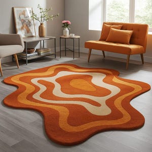Puede incluir: Una alfombra de área de estilo retro con una forma orgánica única. La alfombra presenta un diseño en capas con tonos de naranja, crema y amarillo. La alfombra está colocada sobre un suelo de madera gris claro. La habitación está amueblada con muebles de estilo moderno de mediados de siglo.