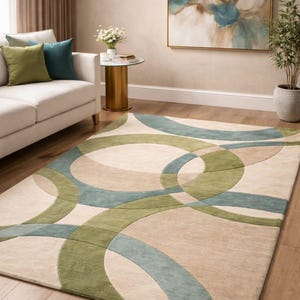 Könnte beinhalten: Beiger Teppich mit einem geometrischen Muster aus sich überlappenden Kreisen in Grün und Blau. Der Teppich liegt auf einem Holzboden in einem Wohnzimmer. Der Raum hat auch ein weißes Sofa, Zierkissen und einen goldenen Beistelltisch.