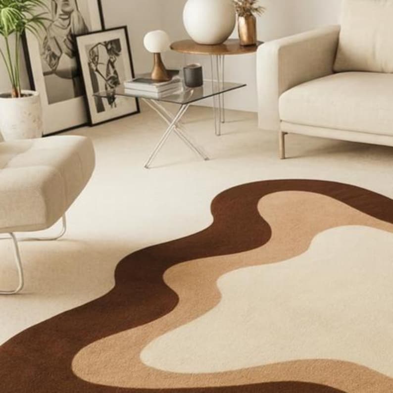 Puede incluir: Un sal&oacute;n moderno con una alfombra color crema con un dise&ntilde;o ondulado en tonos marr&oacute;n y beige. La habitaci&oacute;n incluye un sof&aacute; beige, una mesa auxiliar de cristal y obras de arte enmarcadas. Una planta en maceta y objetos decorativos completan la est&eacute;tica de la habitaci&oacute;n.
