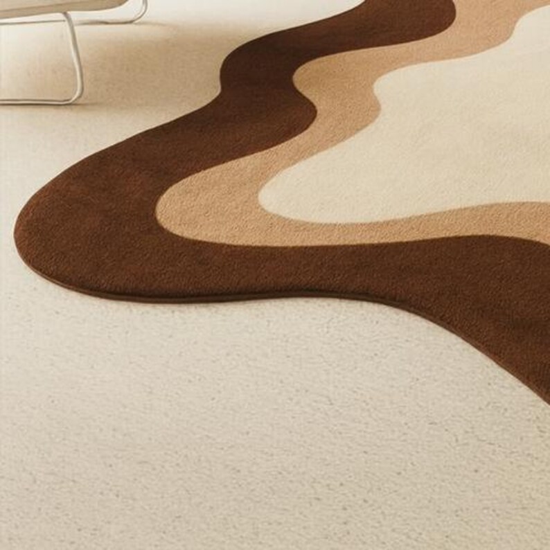 Puede incluir: Una alfombra ondulada marr&oacute;n, beige y crema. La alfombra tiene un dise&ntilde;o retro con un borde marr&oacute;n oscuro y patrones de ondas marrones claros, beige y crema. La alfombra est&aacute; sobre una moqueta color crema.
