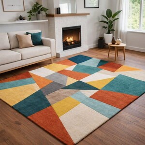 Könnte beinhalten: Ein farbenfroher geometrischer Teppich mit modernem Design. Der Teppich zeigt ein Patchwork aus Dreiecken und anderen Formen in Orange-, Gelb-, Türkis-, Blau-, Grau- und Cremetönen. Der Teppich liegt auf einem Holzboden in einem Wohnzimmer.