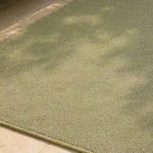 May include: A rectangular, sage green rug with a textured surface. The rug has a subtle, light-colored pattern and a darker green border. The rug is placed on a light-colored tile floor.